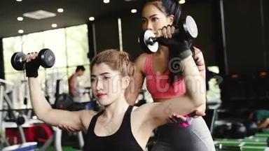 亚洲私人教练指导一位健美女士在健身中与哑铃一起进行举重练习